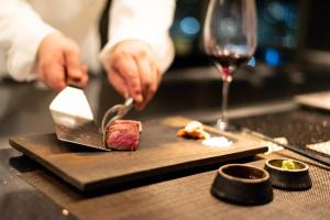 a person cutting a piece of meat on a plate with a glass of wine at Kobe Meriken Park Oriental Hotel in Kobe