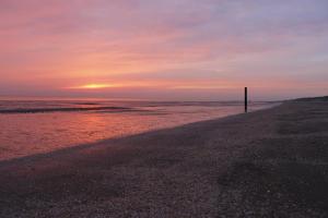 una puesta de sol en la playa con un poste en la arena en De Jongens, en Rockanje