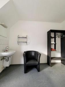 ein Badezimmer mit einem schwarzen Stuhl und einem Waschbecken in der Unterkunft Pension Akropolis in Rellingen