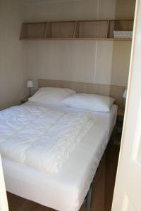 un letto con lenzuola bianche e cuscini sopra di Chalet De Duinberg a IJmuiden