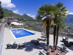 a pool with chairs and palm trees on a patio at Albergo Deva in Riva del Garda