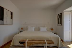 a white bedroom with a large bed with a wooden bench at Solar Dos Mouros in Lisbon