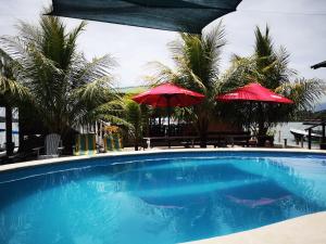 a swimming pool with two red umbrellas and palm trees at Linda Vista in Río Dulce