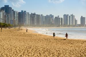 pessoas andando na praia em frente a uma cidade em Hotel Plaza Mar em Vila Velha