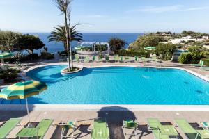 a swimming pool with chairs and an umbrella and the ocean at Hotel Residence Sciaron in Capo Vaticano