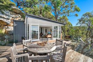 a house with a table and chairs on a deck at Cape Mackerel Cabin with Magic Palm Beach & Pittwater Views in Great Mackerel Beach