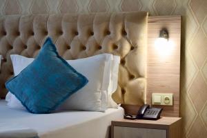 a bed with a blue pillow and a phone on a table at Dostar Inn in Shymkent