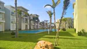 a resort with a pool and palm trees and a rock at F3 Casabay beach sidi rahal vue sur piscine in Sidi Rahal