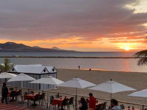 een strand met tafels en witte parasols bij zonsondergang bij OceanFront Flat I by Canary365 in Las Palmas de Gran Canaria
