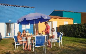 a group of people sitting at a table under an umbrella at Résidence Odalys Le Village des Amareyeurs in Le Château-dʼOléron