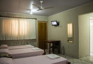 a bedroom with two beds and a desk and a ceiling fan at Hotel Barão Do Rio Branco in Bebedouro