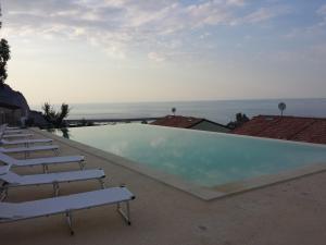a swimming pool with chairs and the ocean in the background at Residence Magarà in Cefalù