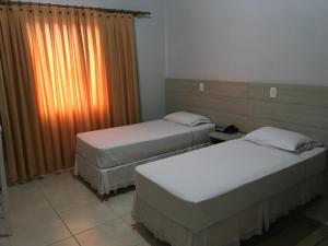 two twin beds in a room with a window at Hotel Faeli in Matelândia