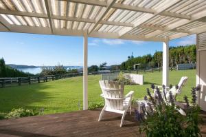 a patio with two white chairs and a field of grass at Hydrangea Cottage in Katikati
