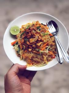 eine Person, die einen Teller Essen mit einer Schüssel Nudeln hält in der Unterkunft Adang Sea Divers & Eco Lodge in Ko Lipe