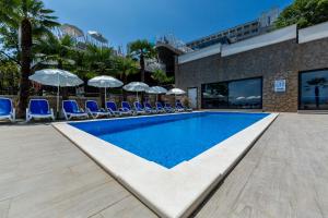 a swimming pool with blue chairs and umbrellas at Hotel Domino in Opatija