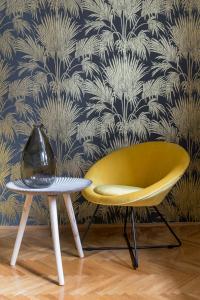 a yellow chair and a side table in front of a wallpaper at Central Apartman in Budapest