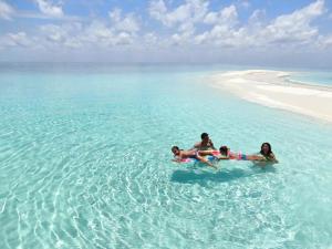 three people laying in the water on a beach at Villa Kudì Maldives Guest House Thulusdhoo in Thulusdhoo
