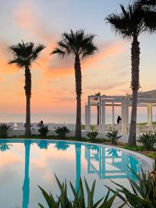 a pool with palm trees in front of the ocean at Capovaticano Resort Thalasso Spa in Capo Vaticano