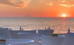 a sunset over the ocean with white chairs on the beach at Capovaticano Resort Thalasso Spa in Capo Vaticano