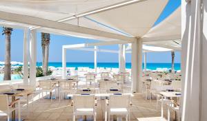 a restaurant with white tables and chairs and the ocean at Capovaticano Resort Thalasso Spa in Capo Vaticano
