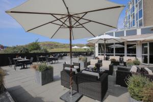 a patio with tables and chairs and an umbrella at Fletcher Hotel Restaurant Zeeduin in Wijk aan Zee