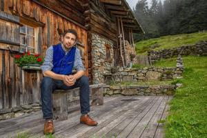 a man sitting on a bench in front of a cabin at Pension Edelweiss in Gargellen