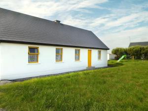 a white house with orange windows and a green field at Suncatchers Upper Fierd Kilbaha Kilkee in Kilrush