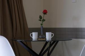 a vase with a flower on a glass table with two cups at Birchwood Spa Motel in Rotorua