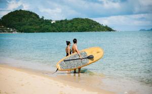 two people sitting on the beach with a surfboard at Anantara Bophut Koh Samui Resort in Bophut