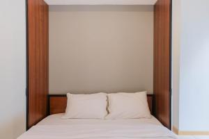 a bed with white sheets and a wooden headboard at Comfortable 2BR Apartment Serpong M-Town Residence By Travelio in Tangerang +12 photos