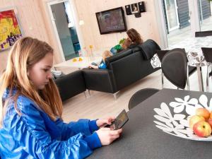 a young girl sitting at a table looking at a cell phone at 24 person holiday home in Bl vand in Blåvand