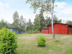 a red barn and a tree in a yard at Two-Bedroom Holiday home in Væggerløse 24 in Marielyst