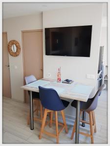 a dining room table with chairs and a television on the wall at -CAPCIR- Standing, cosy, 50m de la plage, parking, wifi in Canet-en-Roussillon