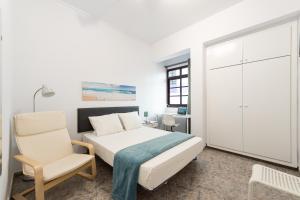 een witte slaapkamer met een bed en een stoel bij CoolivingC in Las Palmas de Gran Canaria