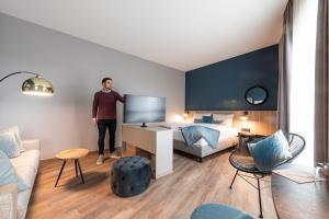a man standing in a hotel room with a bed at HARBR. hotel Heilbronn in Heilbronn
