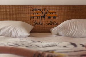 een bed met twee kussens en een bord aan de muur bij Hosteria Alpaka Quilotoa in Quilotoa