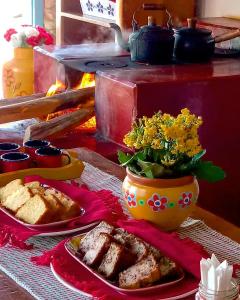 uma mesa com um prato de comida e um vaso de flores em Vila das Artes Chales em Lavras Novas