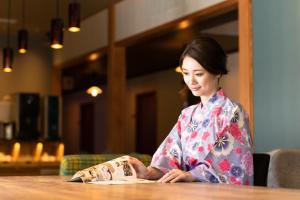 Una donna seduta a un tavolo che guarda una borsa di Onsen Guest House Aobato no Su a Matsue