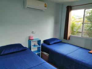 a bedroom with two blue beds and a window at Canaan in Kanchanaburi