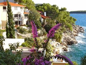 a house with purple flowers in front of the water at Rooms Tepli Bok in Primošten