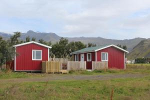 twee rode huizen in een veld met bergen op de achtergrond bij Núpakot in Steinar