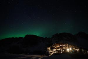 aurora świeci na niebie nad chatą w obiekcie Mulakot Cosy Cabins w mieście Borgarnes