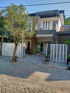 a house with a white fence and a tree at Kalandra Guest House in Ponorogo