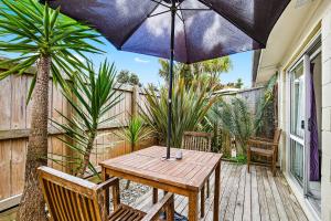 - une table en bois avec un parasol sur la terrasse dans l'établissement Waipu Cove Resort, à Waipu