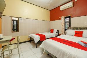 a room with two beds and a table and a desk at RedDoorz Syariah near Ciledug Station in Cirebon