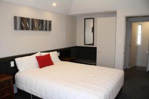 1 dormitorio con cama blanca y almohada roja en Birchwood Manor, en Invercargill