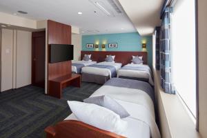 a hotel room with three beds and a flat screen tv at HOTEL MYSTAYS Yokohama in Yokohama