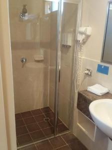 a shower with a glass door next to a sink at Desert Sand Motor Inn in Broken Hill