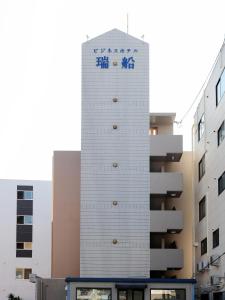 a tall white building with a sign on it at Tabist Rays Hotel Suisen in Miyazaki
